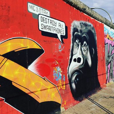 A weary ape with a speech bubble reading "Destroy all smartphones", painted on a red wall beside part of a large yellow shape.