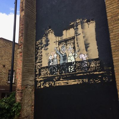 Stencilled characters standing on a painted balcony against a rough black-and-tan dark wall.