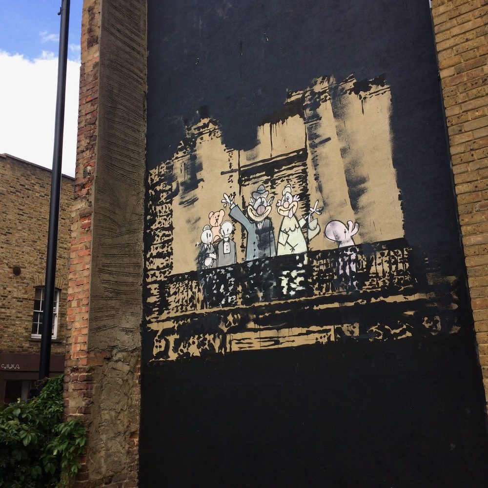 Stencilled characters standing on a painted balcony against a rough black-and-tan dark wall.