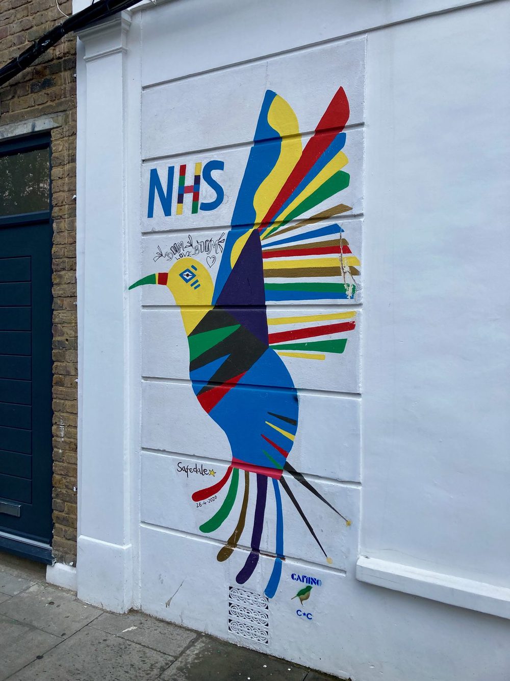 A colourful abstract bird with "NHS" lettering beside it, painted on a white wall.