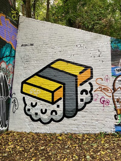 A tamago sushi piece with a yellow top and a simple stylised face, painted on a white brick wall.