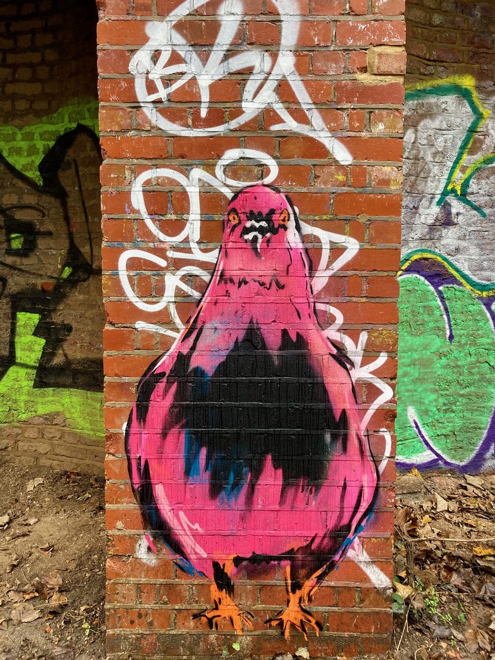 A plump pink stylised pigeon painted on a red brick pillar over white graffiti.