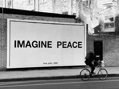 A black-and-white billboard-style artwork reading "Imagine peace" and "love, yoko 2022", with a cyclist passing by.