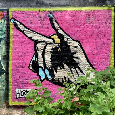 A large Lichtenstein-style hand making a devil-horns gesture, with Ben-Day dots, painted on a pink wall; signed "Horace".