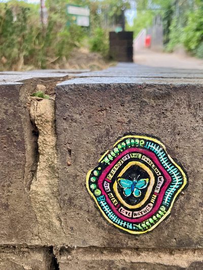 A blue butterfly at the centre of a small circular painted sticker on a rough stone ledge, with text around the border including "Love nature".