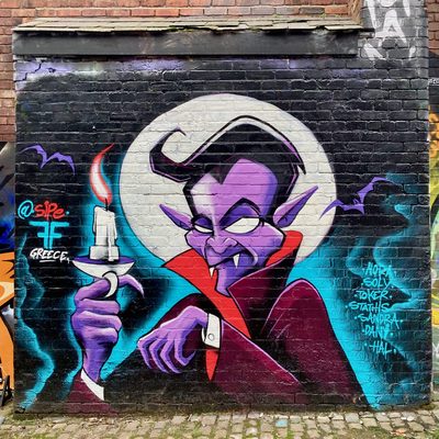 A purple vampire holding a lit candle in front of a full moon, painted on a brick wall.