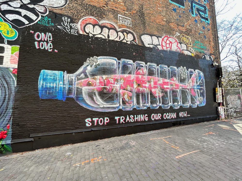 A plastic bottle with fish inside and the words "Stop trashing our ocean now." painted as a large wall mural.