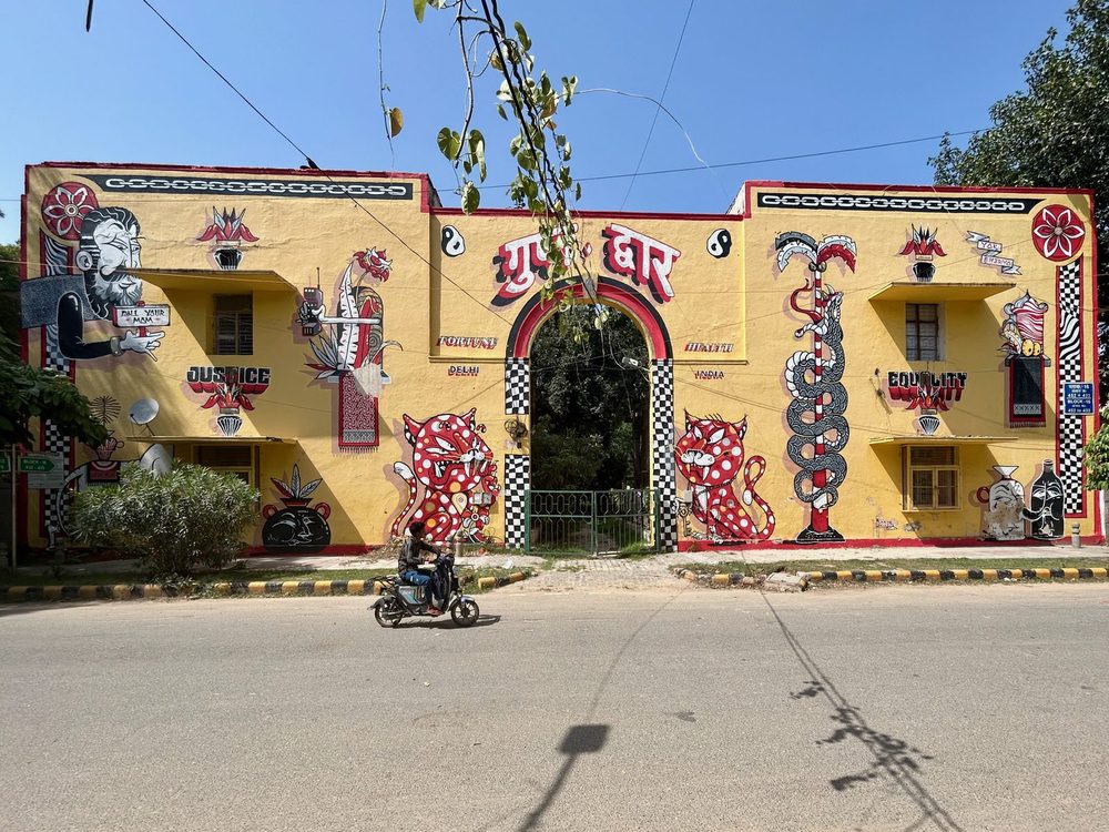 Colourful murals of animals, symbols, and words including "justice", "fortune", "health", and "equality", covering a yellow building facade.