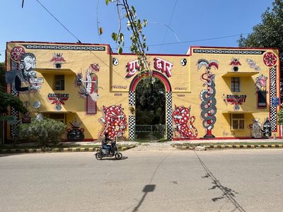 Colourful murals of animals, symbols, and words including "justice", "fortune", "health", and "equality", covering a yellow building facade.