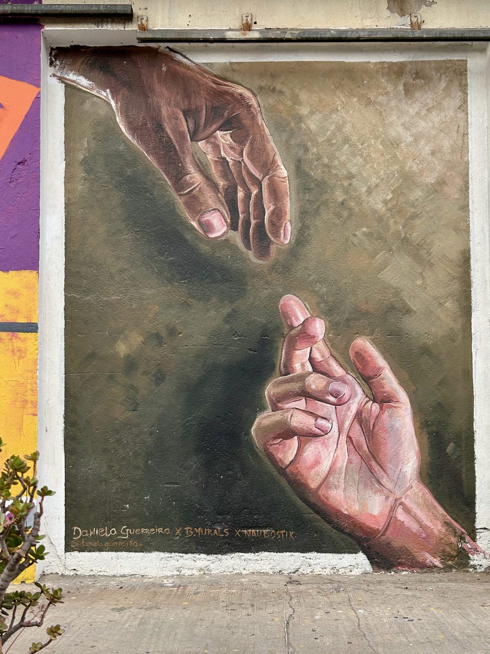 Two realistic painted hands reaching toward each other against a muted grey-green background.