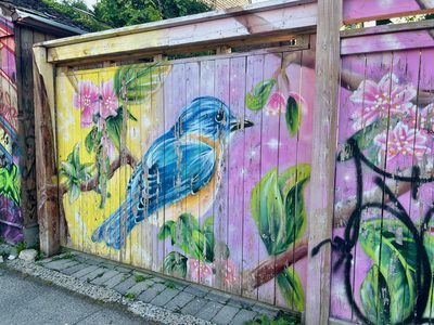 A blue bird perched among pink blossoms and green leaves, painted on a weathered wooden fence.