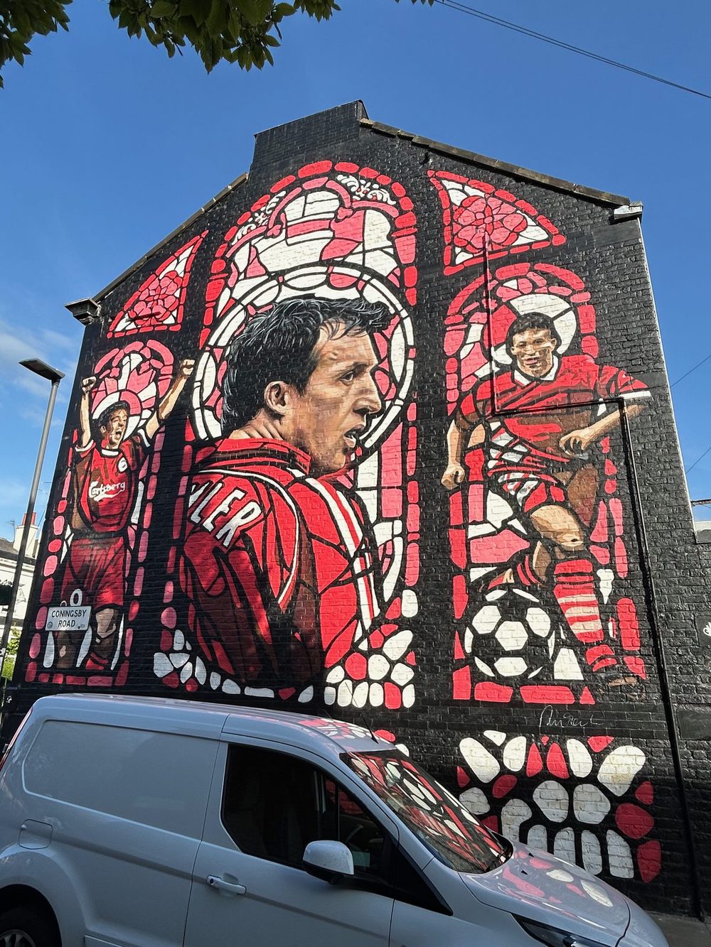 Robbie Fowler in a red Liverpool kit, painted in red-and-white stained-glass-style panels on a black brick wall.