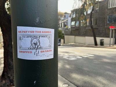 A sticker on a pole reading "We pay for the bombs dropped on Gaza" above a stylised dollar bill marked "X Billion Dollars" and the question "Do you want to fund genocide?"