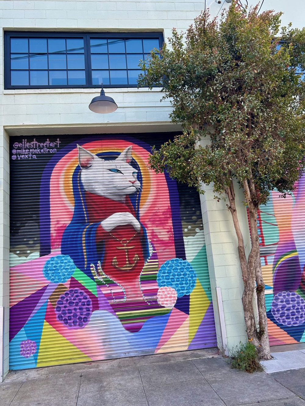 A white cat in a red robe and blue headscarf, framed by bright circular shapes, painted on a colourful garage door.