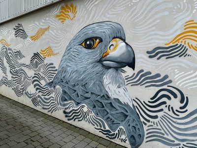 A grey falcon head surrounded by flowing grey, white, and yellow line patterns, painted on a pale wall.