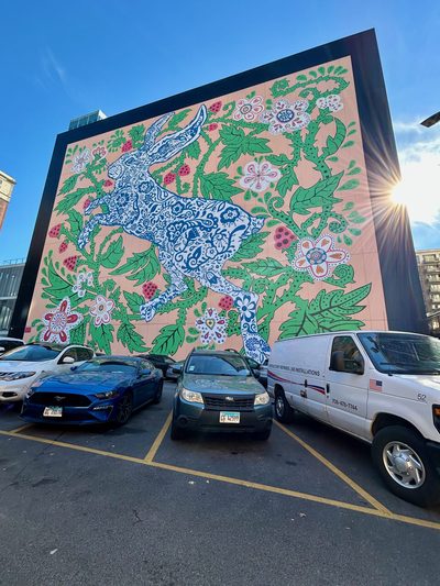 A blue-and-white patterned hare among green vines, pink berries, and flowers, painted as a huge building mural.