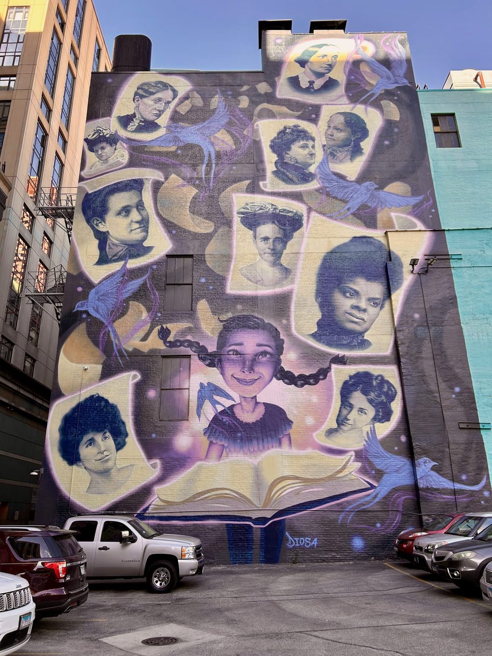 Portraits of people emerging from an open book, with purple light trails and blue birds around them, painted as a tall mural; signed "DIOSA".