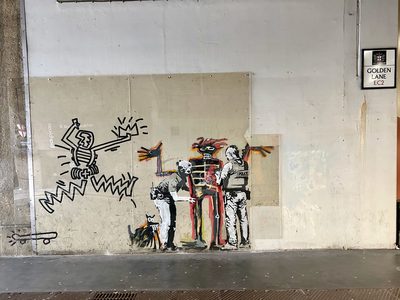 A Banksy-style stencil of two police officers searching a Basquiat-style crown-headed figure, with a Keith Haring-style line figure to the left, on a wall protected by clear panels on Golden Lane EC2.